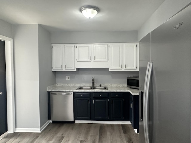 kitchen with stainless steel appliances, white cabinetry, a sink, wood finished floors, and dark cabinetry