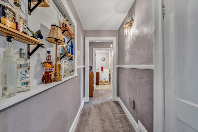 corridor featuring light carpet, a textured wall, and baseboards