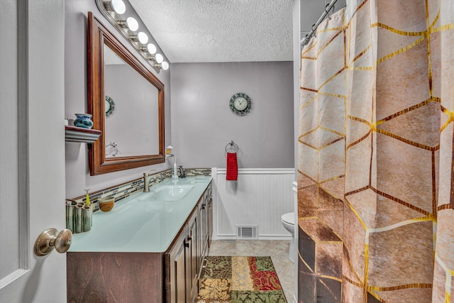 bathroom featuring a wainscoted wall, visible vents, toilet, a textured ceiling, and vanity