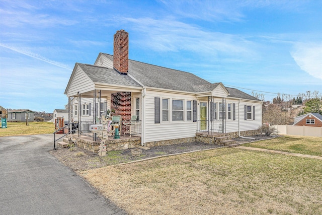 bungalow-style home with a shingled roof, fence, a chimney, and a front lawn