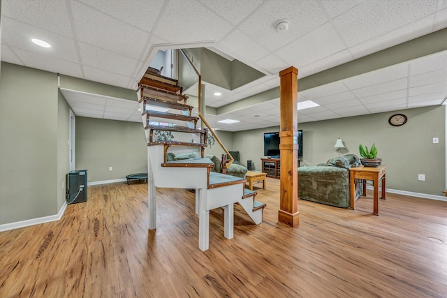 finished basement with stairway, a drop ceiling, wood finished floors, and baseboards