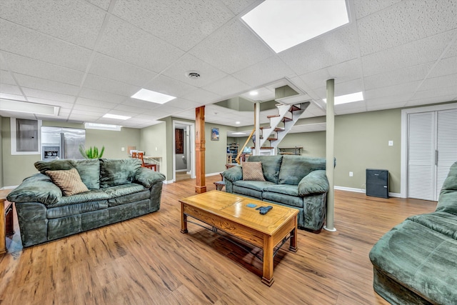 living area featuring baseboards, visible vents, a drop ceiling, wood finished floors, and stairs