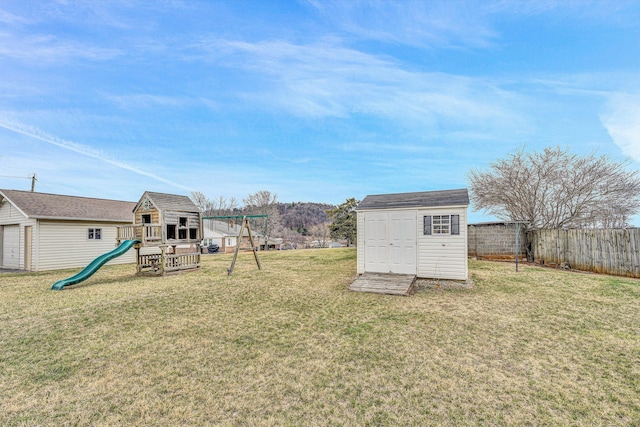 view of yard featuring an outbuilding, a storage unit, a playground, and a fenced backyard