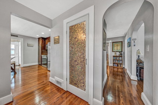 corridor featuring visible vents, arched walkways, baseboards, wood-type flooring, and recessed lighting