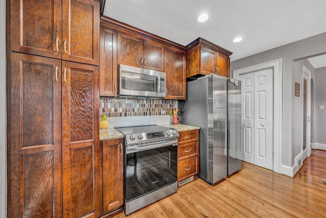 kitchen featuring decorative backsplash, appliances with stainless steel finishes, light wood-style floors, light stone countertops, and baseboards