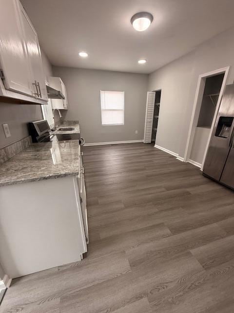 kitchen with wall chimney exhaust hood, baseboards, white cabinetry, and dark wood finished floors