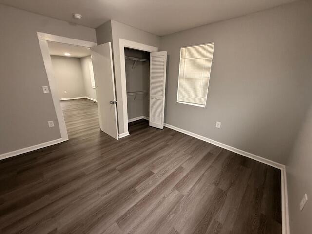 unfurnished bedroom featuring a closet, baseboards, and dark wood-type flooring