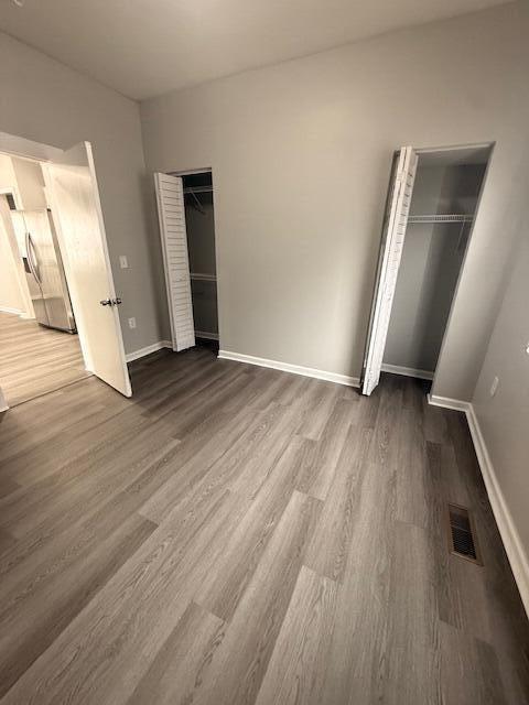 unfurnished bedroom featuring visible vents, dark wood finished floors, stainless steel refrigerator with ice dispenser, and baseboards