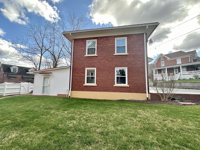 back of house featuring brick siding, a lawn, and fence