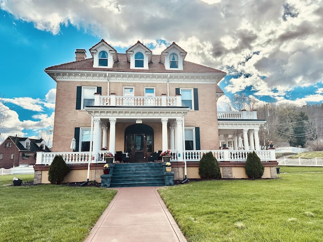 view of front facade featuring brick siding, a balcony, fence, a porch, and a front yard