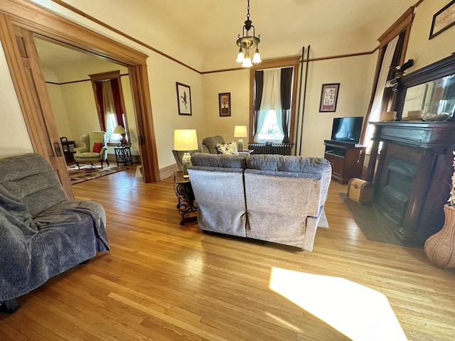 living area with a chandelier, light wood-type flooring, a glass covered fireplace, and crown molding