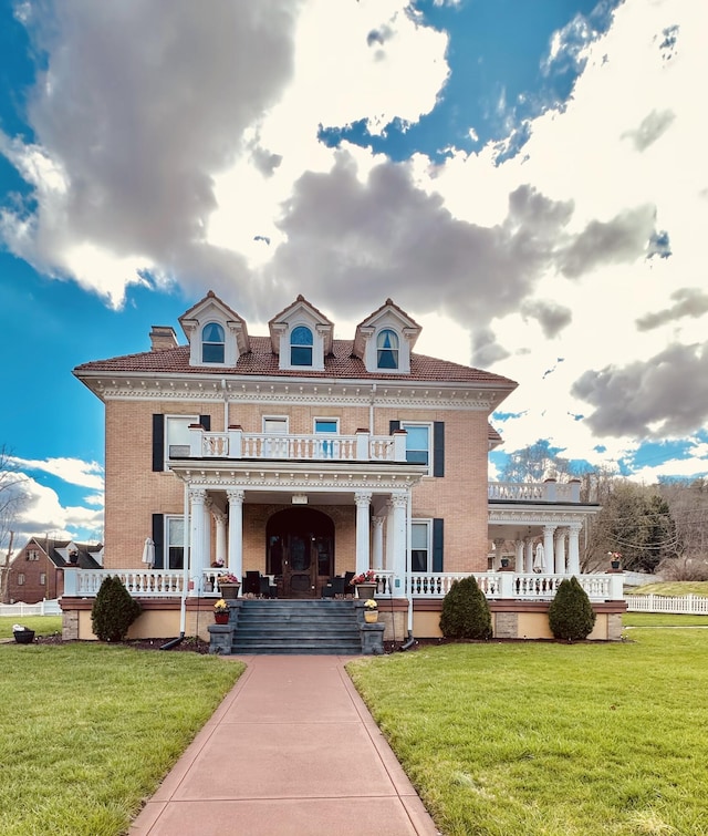 colonial inspired home with a balcony, brick siding, covered porch, and a front yard