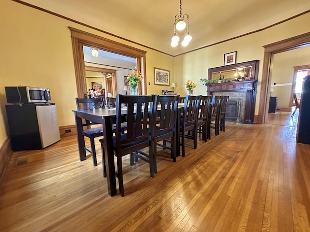 dining room with baseboards, hardwood / wood-style flooring, ornamental molding, a fireplace, and a chandelier