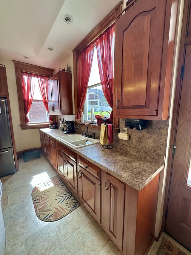 kitchen featuring a sink, baseboards, freestanding refrigerator, tasteful backsplash, and brown cabinetry