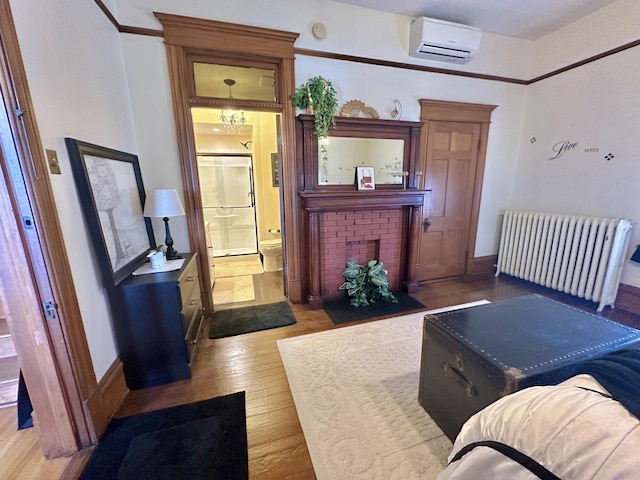 living room with a wall unit AC, radiator, a brick fireplace, wood finished floors, and a chandelier