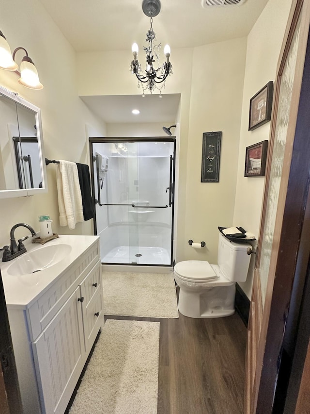 full bathroom with a stall shower, toilet, wood finished floors, an inviting chandelier, and vanity