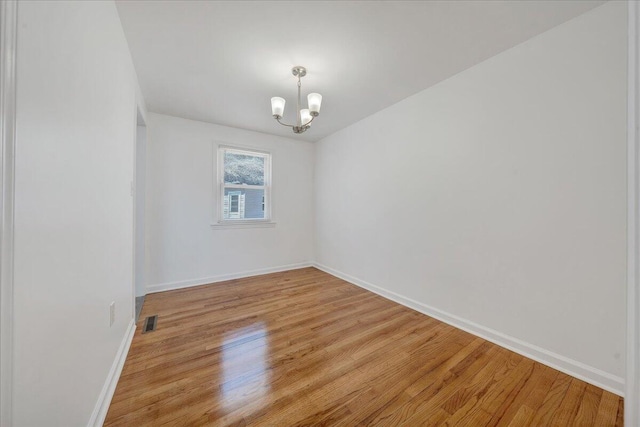 spare room featuring visible vents, a notable chandelier, light wood-style floors, and baseboards