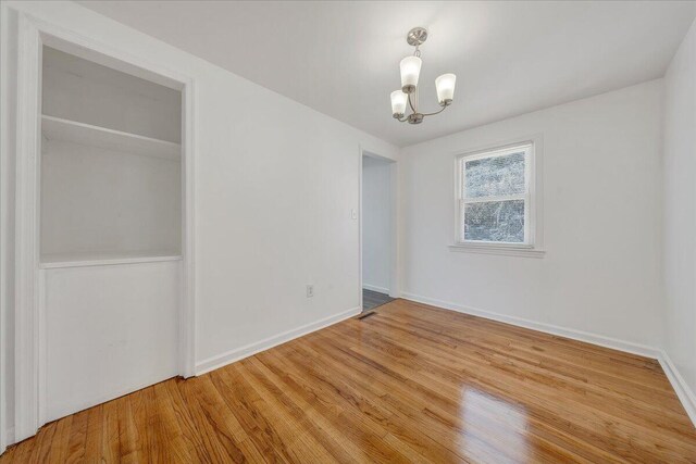 spare room with wood finished floors, baseboards, and a chandelier