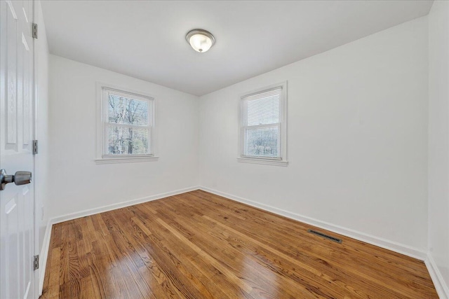 unfurnished room featuring a wealth of natural light, visible vents, baseboards, and wood finished floors