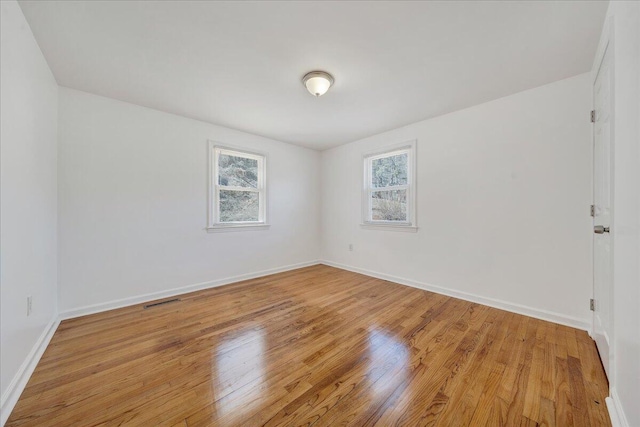 empty room with visible vents, light wood-type flooring, and baseboards