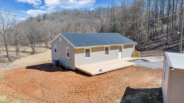 exterior space featuring a deck, central air condition unit, a forest view, and metal roof