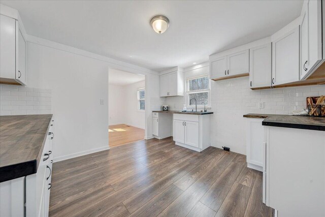 kitchen with dark wood finished floors, a sink, decorative backsplash, white cabinetry, and dark countertops