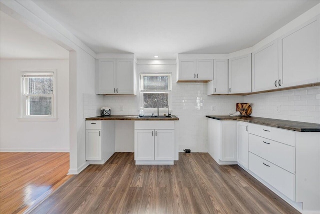 kitchen with dark wood-style floors, a sink, white cabinetry, dark countertops, and tasteful backsplash