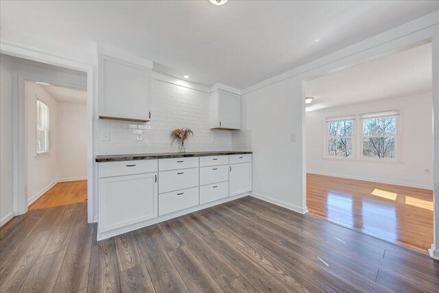 kitchen with decorative backsplash, dark countertops, dark wood finished floors, and white cabinetry