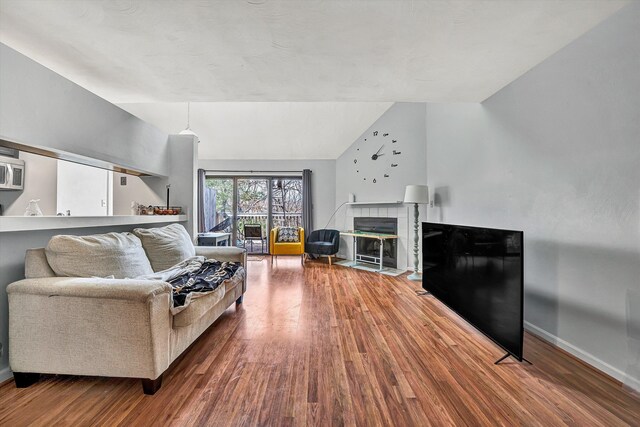 living area featuring baseboards, lofted ceiling, wood finished floors, and a tile fireplace