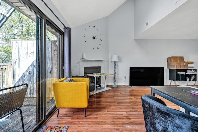 living room with visible vents, baseboards, a tiled fireplace, lofted ceiling, and wood finished floors