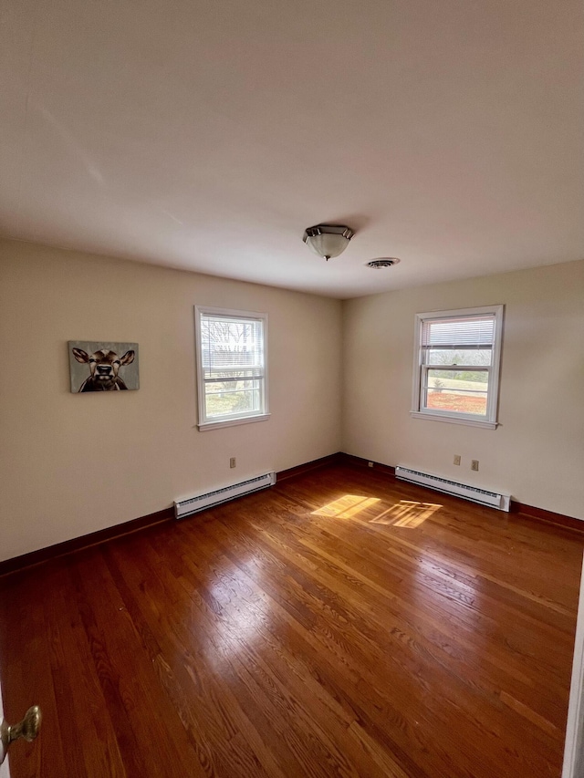 spare room with a baseboard heating unit, dark wood finished floors, plenty of natural light, and baseboard heating