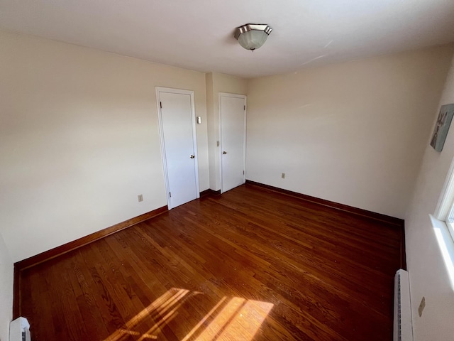 empty room featuring a baseboard heating unit, dark wood-type flooring, and baseboards