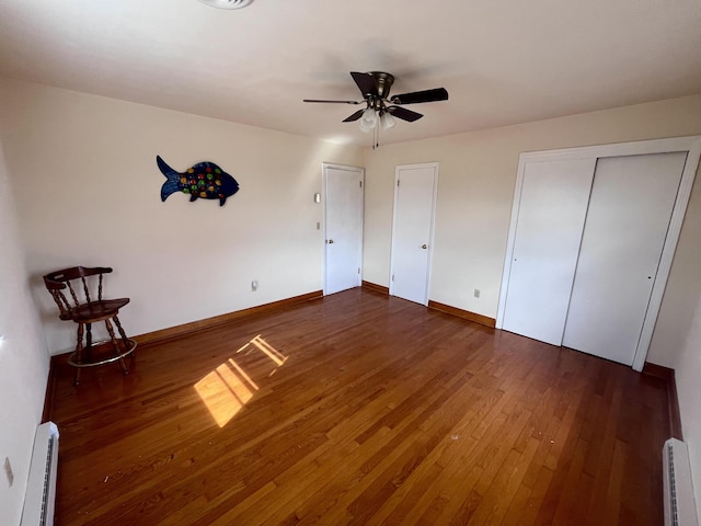 unfurnished bedroom with multiple closets, a baseboard radiator, wood-type flooring, ceiling fan, and baseboards