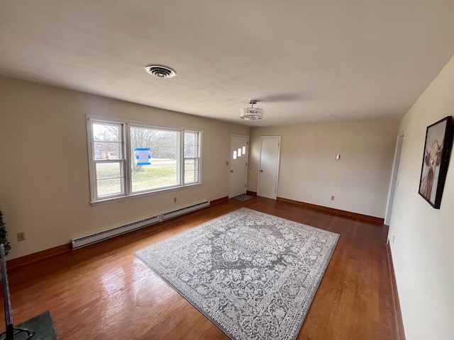 unfurnished living room featuring a baseboard heating unit, visible vents, baseboards, and wood finished floors