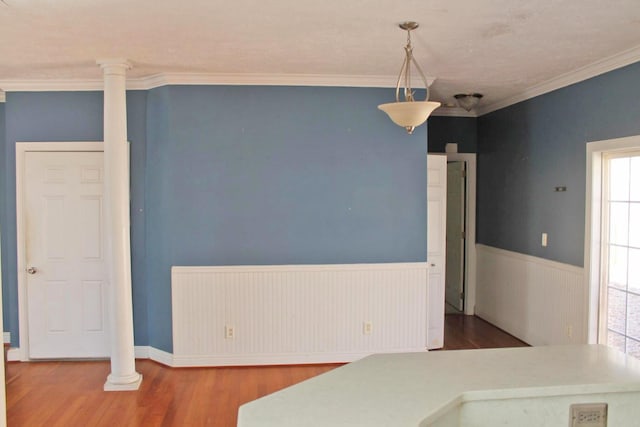 unfurnished dining area with ornamental molding, wainscoting, wood finished floors, and decorative columns