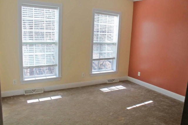 carpeted empty room featuring plenty of natural light, visible vents, and baseboards