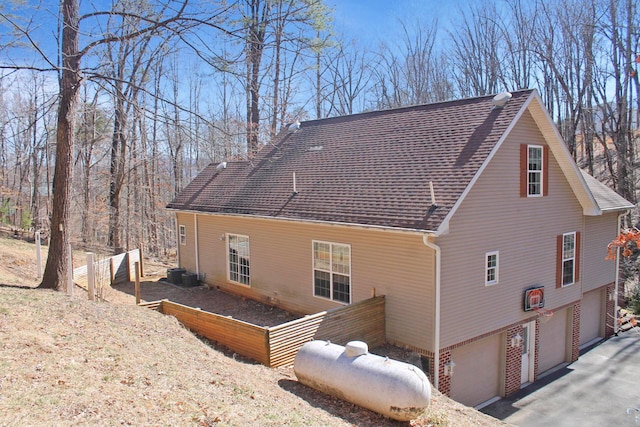 view of property exterior featuring a garage, a garden, fence, and roof with shingles