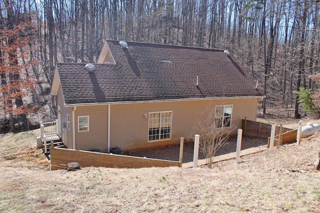 view of property exterior with a shingled roof, fence, and a wooded view