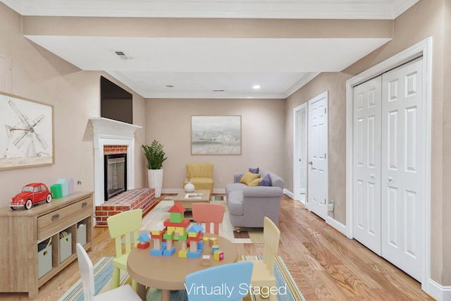 recreation room featuring light wood finished floors, baseboards, a fireplace, and ornamental molding