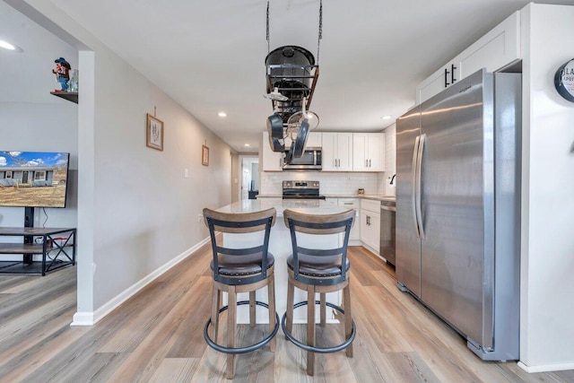 kitchen featuring light wood-style flooring, white cabinetry, appliances with stainless steel finishes, decorative backsplash, and a center island