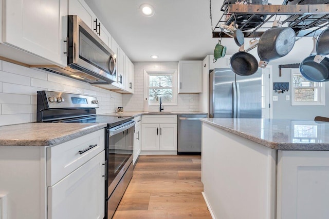 kitchen featuring stainless steel appliances, tasteful backsplash, light wood-style floors, white cabinetry, and a sink