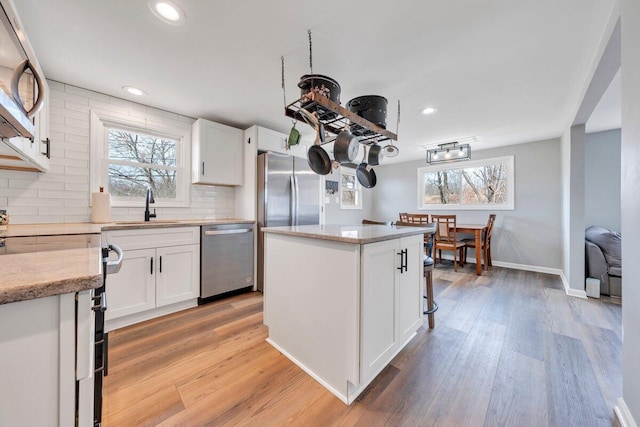 kitchen with light wood-style flooring, decorative backsplash, appliances with stainless steel finishes, white cabinets, and a sink