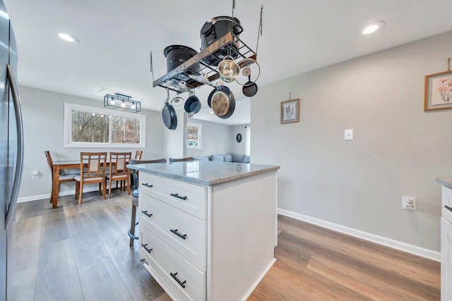 kitchen with light stone counters, freestanding refrigerator, baseboards, and light wood finished floors