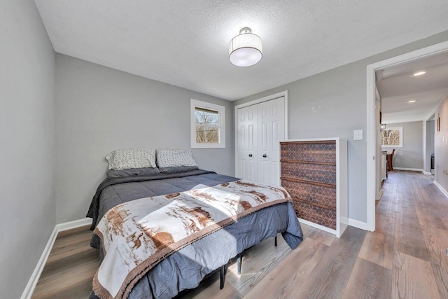 bedroom featuring a closet, a textured ceiling, baseboards, and wood finished floors