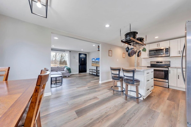 kitchen featuring stainless steel appliances, a kitchen island, light wood-style floors, white cabinets, and decorative backsplash