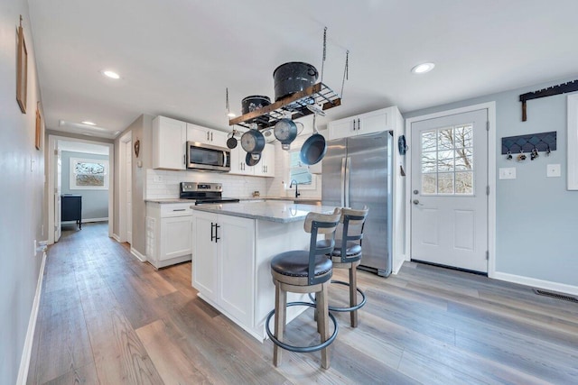 kitchen featuring light wood finished floors, white cabinetry, stainless steel appliances, and decorative backsplash