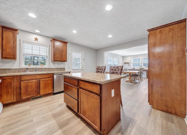 kitchen with visible vents, a kitchen island, stainless steel dishwasher, light wood-style floors, and a sink