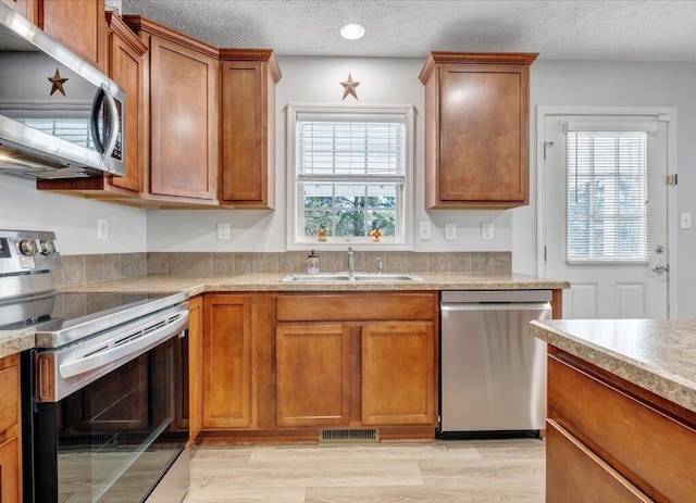 kitchen featuring appliances with stainless steel finishes, plenty of natural light, brown cabinets, and a sink