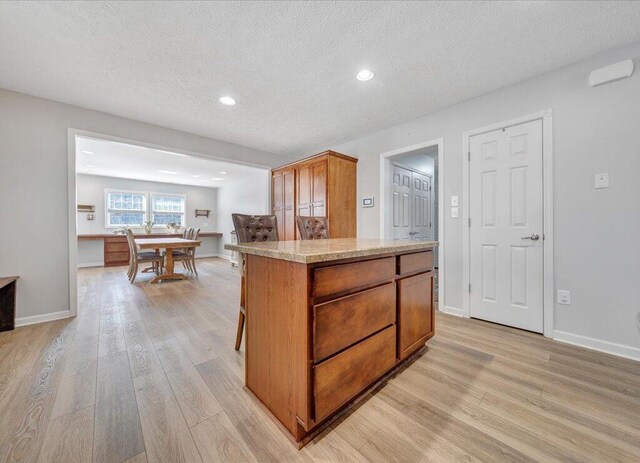 kitchen featuring baseboards, light wood-style flooring, brown cabinets, a center island, and a textured ceiling