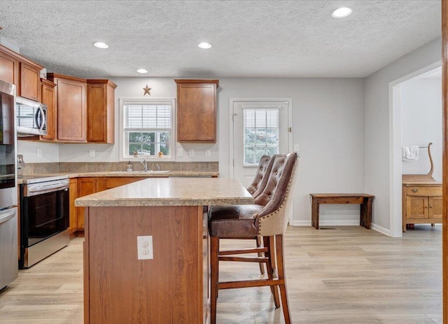 kitchen featuring light wood finished floors, a kitchen island, appliances with stainless steel finishes, and a wealth of natural light